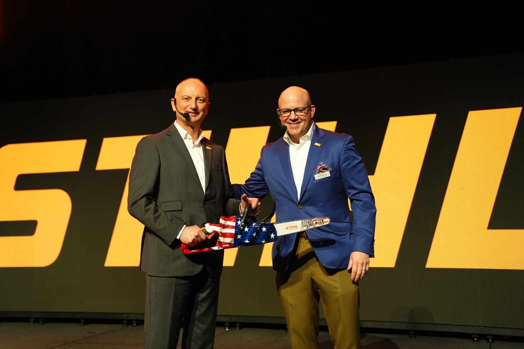 Tohtori Nikolas Stihl (vasemmalla) ja Chris Keffer, STIHL Inc:n toimitusjohtaja Yhdysvalloissa, esittelevät Yhdysvaltain lipulla koristellun juhlasahan.